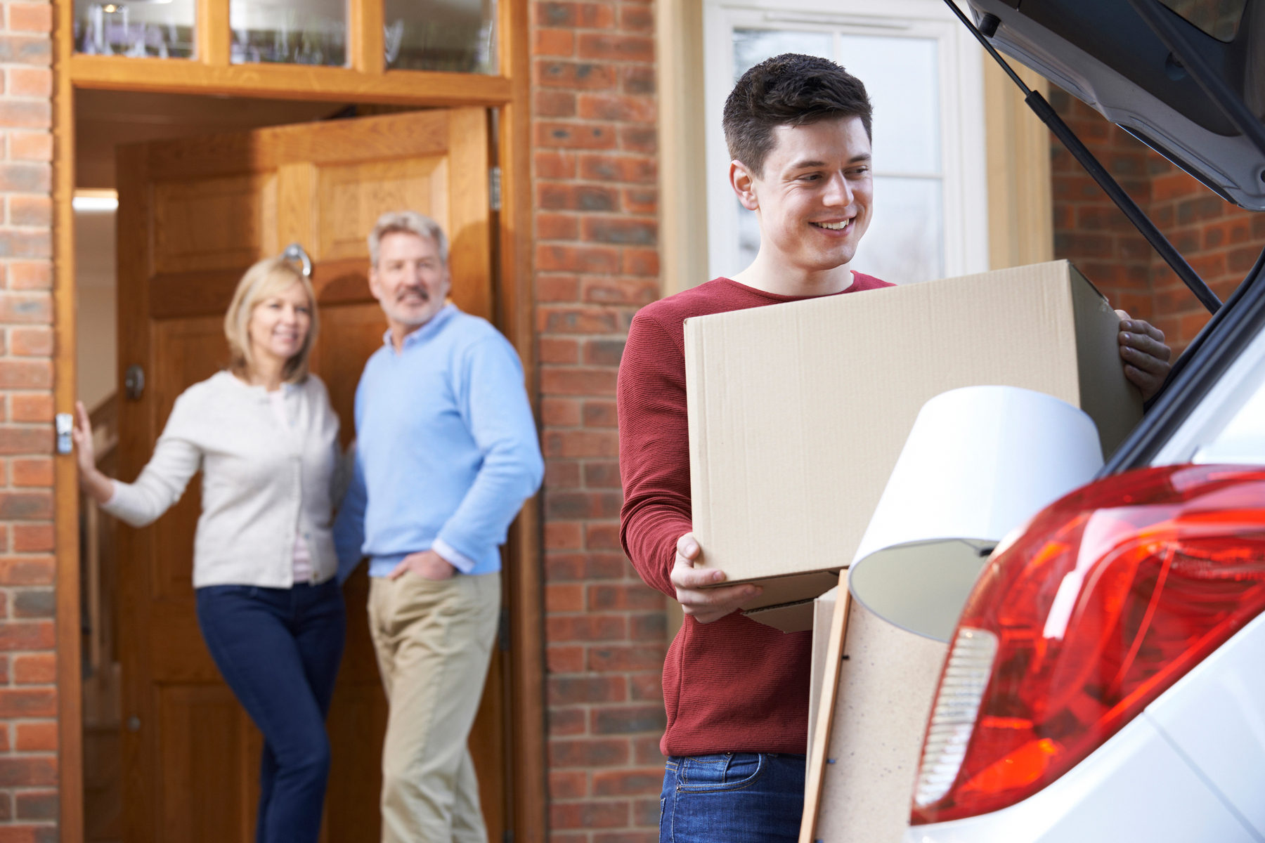 son loading boxes into car while parents stand by