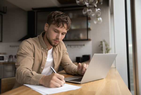 young man checking paperwork while using laptop