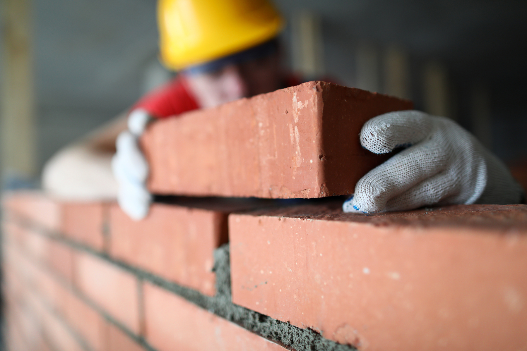 A builder carefully lays a brick on a wall