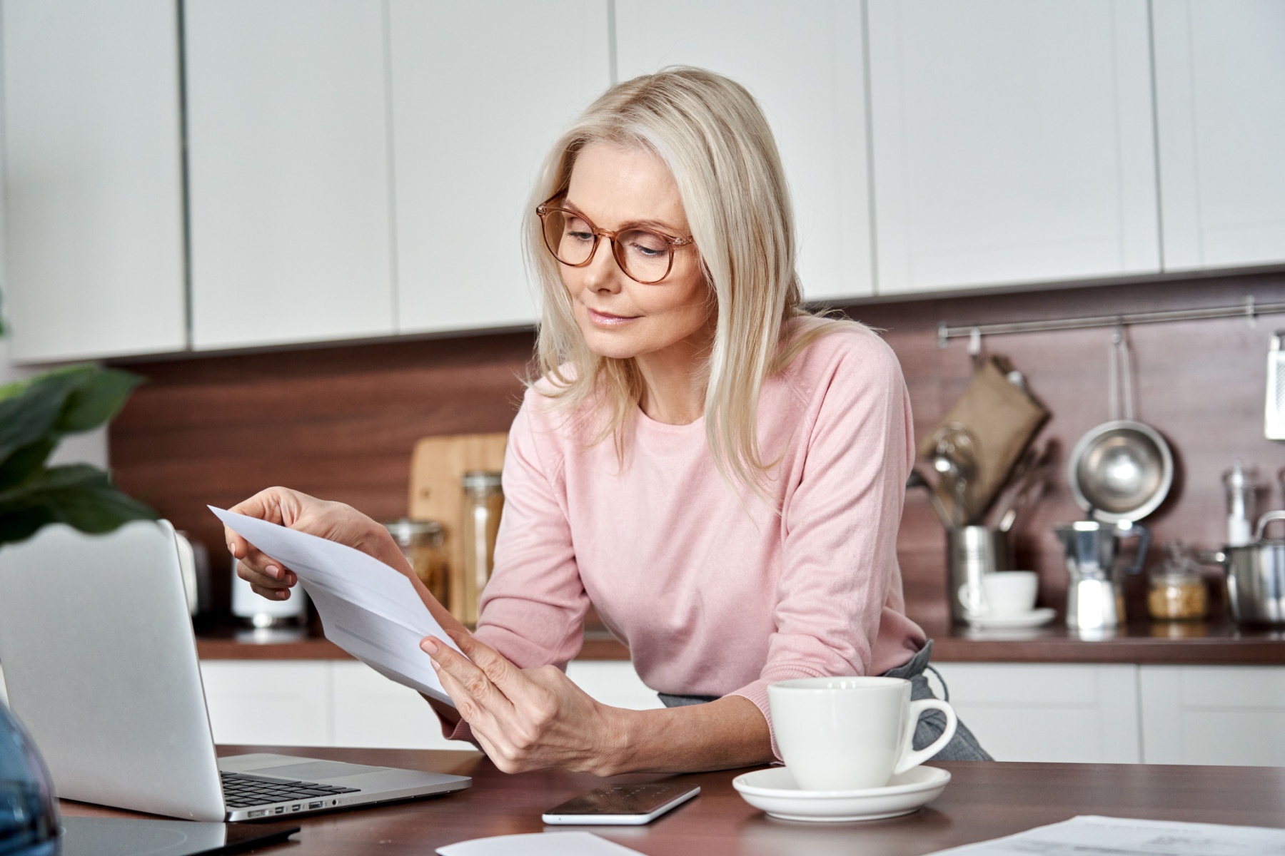 Middle-aged woman looks at documents in front of laptop
