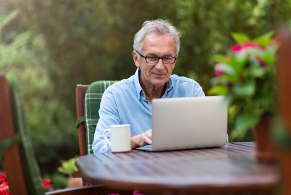 An older man sits in the garden with a laptop